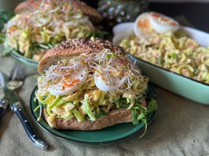 broodje ham prei salade met ei en kerrie geserveerd met verse kiemgroenten op een rond bord