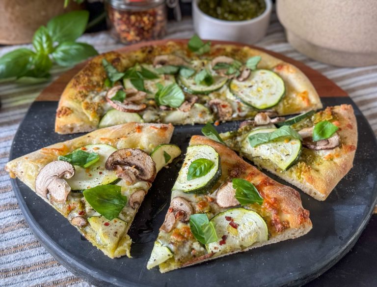 pizza met pistache pesto en kaas geserveerd op een ronde plank en bestrooid met verse basilicum