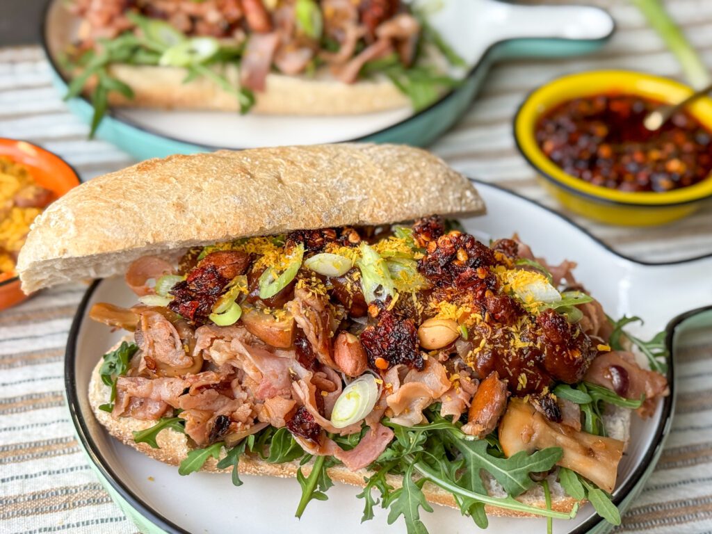 broodje warme beenham met pindasaus met crispy chili olie, seroendeng, rucola en fijngesneden bosui