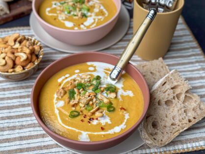 een kom vol heerlijke bloemkoolsoep met zoete aardappel, gele curry en afgetopt met bosui, cashewnoten en chilivlokken