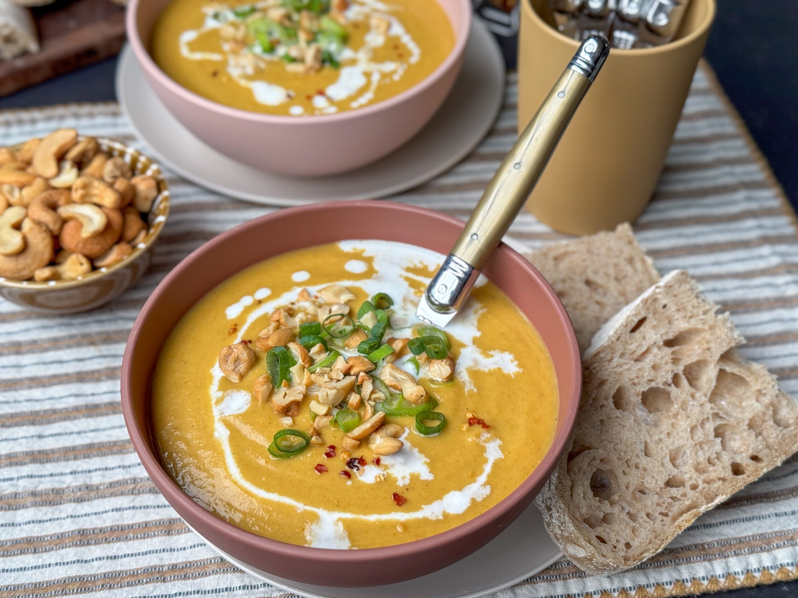 een kom vol heerlijke bloemkoolsoep met zoete aardappel, gele curry en afgetopt met bosui, cashewnoten en chilivlokken