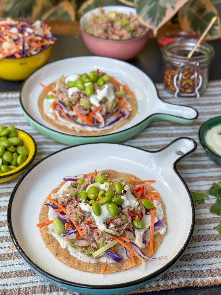 tostada met tonijnsalade, sojaboontjes, avocado en frisse limoen-yoghurtdressing geserveerd op een rond bord.