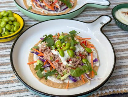 tostada met tonijn en avocado, sojaboontjes en koolmix geserveerd met een frisse limoen – yoghurtdipsaus geserveerd op een bord.