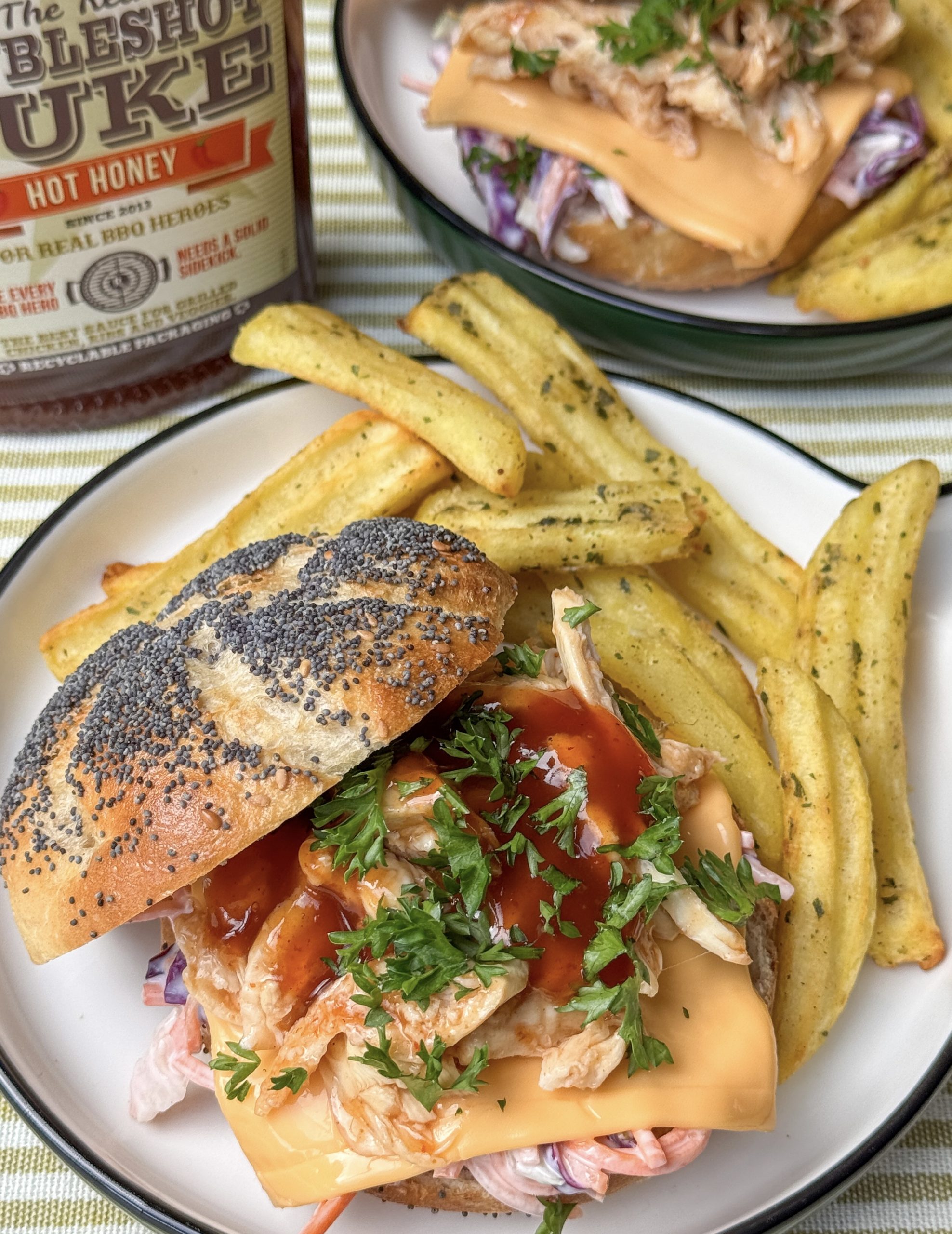 pulled chicken broodje met hot honey bbq saus, geserveerd met frietjes op een bord
