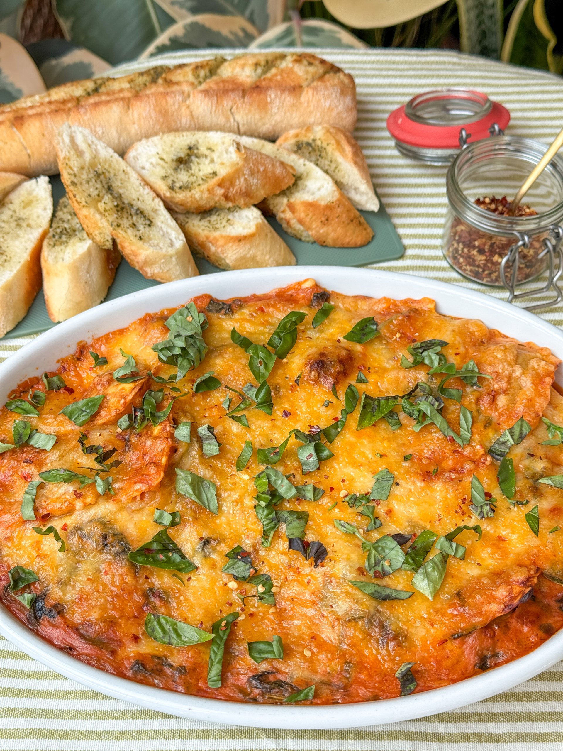 ravioli ovenschotel met spinazie in romige tomatensaus, in witte schaal met gesmolten kaas en basilicum