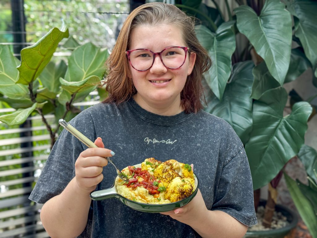 geroosterde bloemkool uit de oven vastgehouden door Beaudine op rond bord met aardappelpuree en spekjes