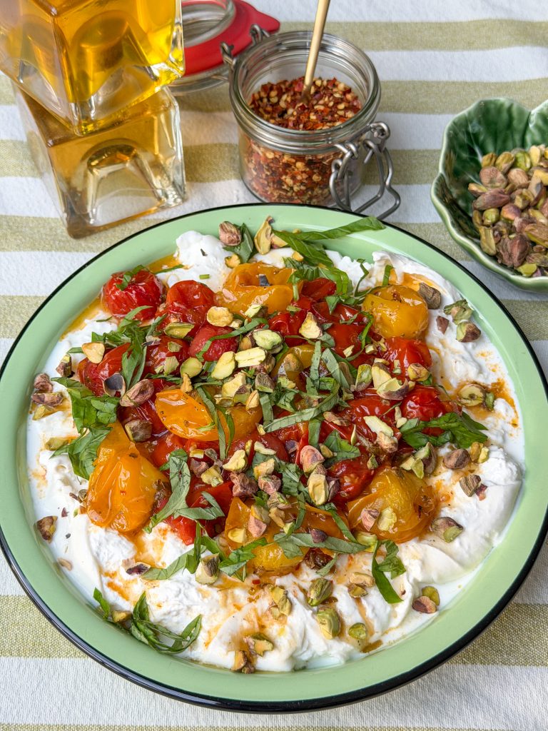 burrata dip met geroosterde tomaten, basilicum en pistachenootjes op rond bord