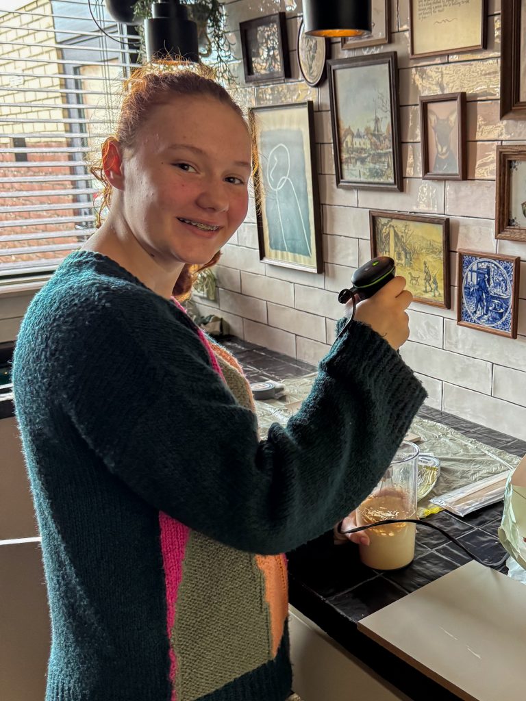 Amaranthe in de keuken terwijl ze met een kleine mixer haar drankje klaarmaakt.