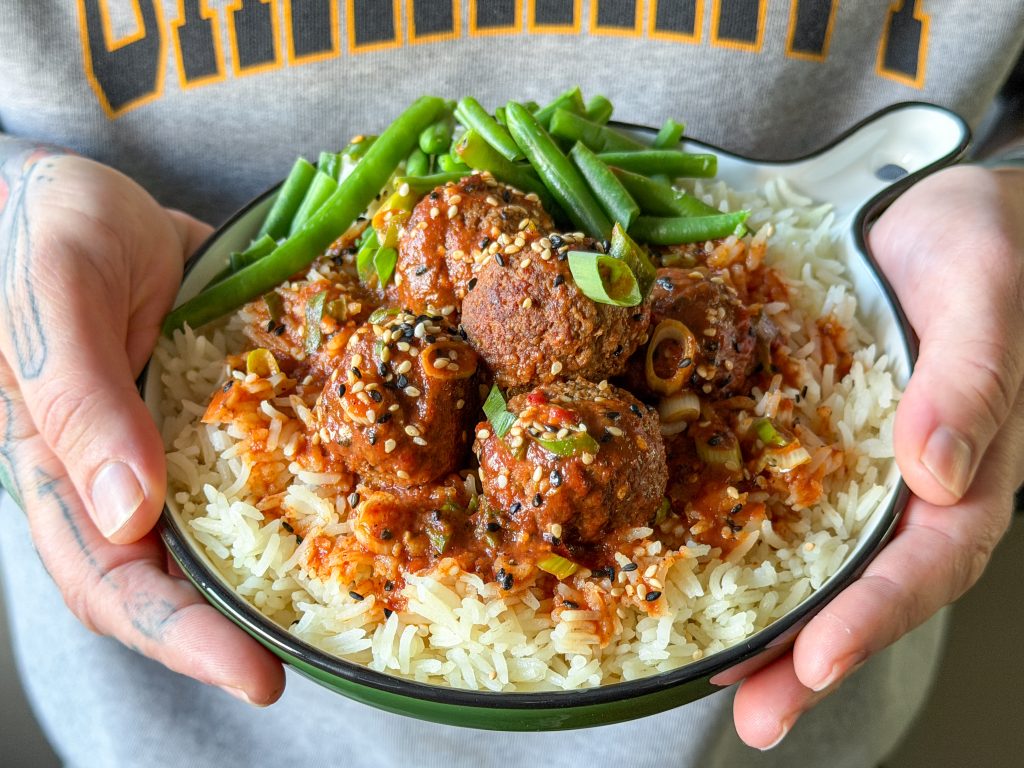 bord met gehaktballetjes in zoet zure saus en rijst die in twee handen wordt vastgehouden