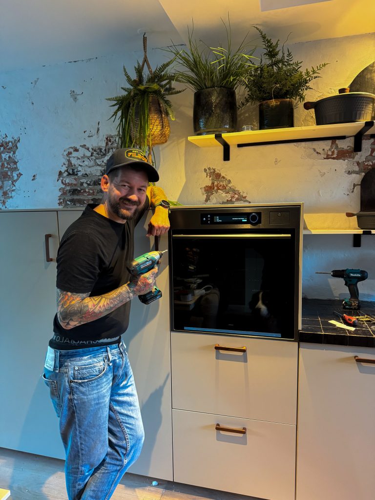 Jan Willem lachend naast de net geplaatste oven met gereedschap op het aanrecht.