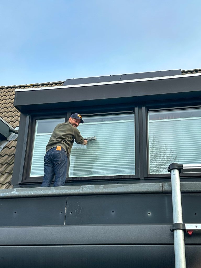 Jan Willem die de bovenramen van het huis wast.