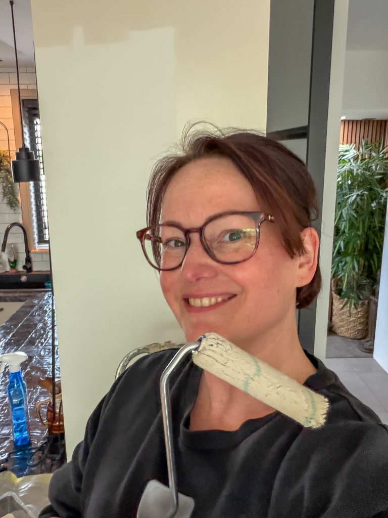 Marie-Louise lacht terwijl ze met een verfroller een muur aan het verven is in de keuken.