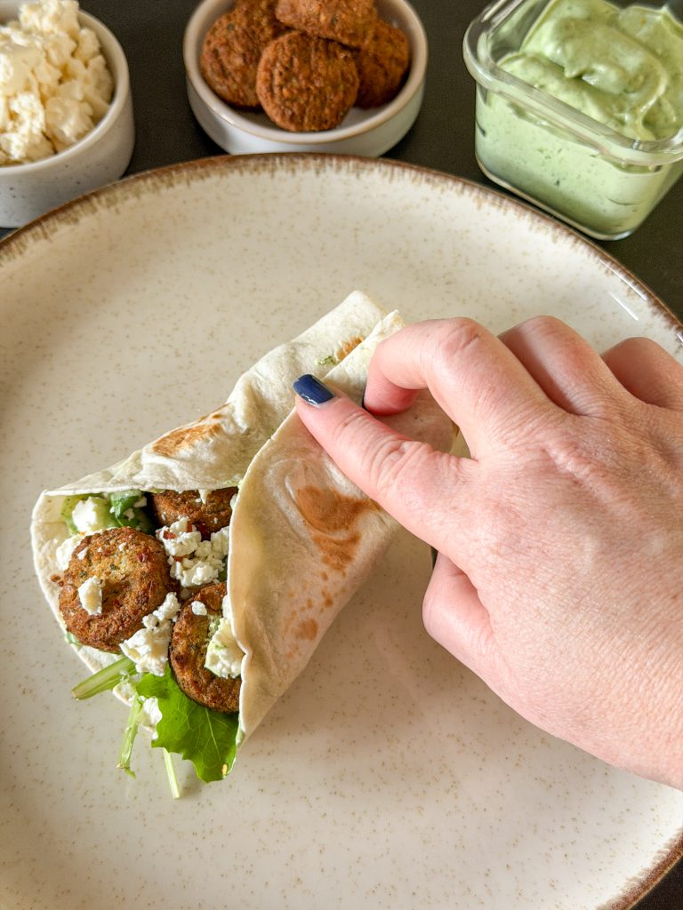 Opgerolde wrap met falafel, feta en sla op bord, klaar om te eten