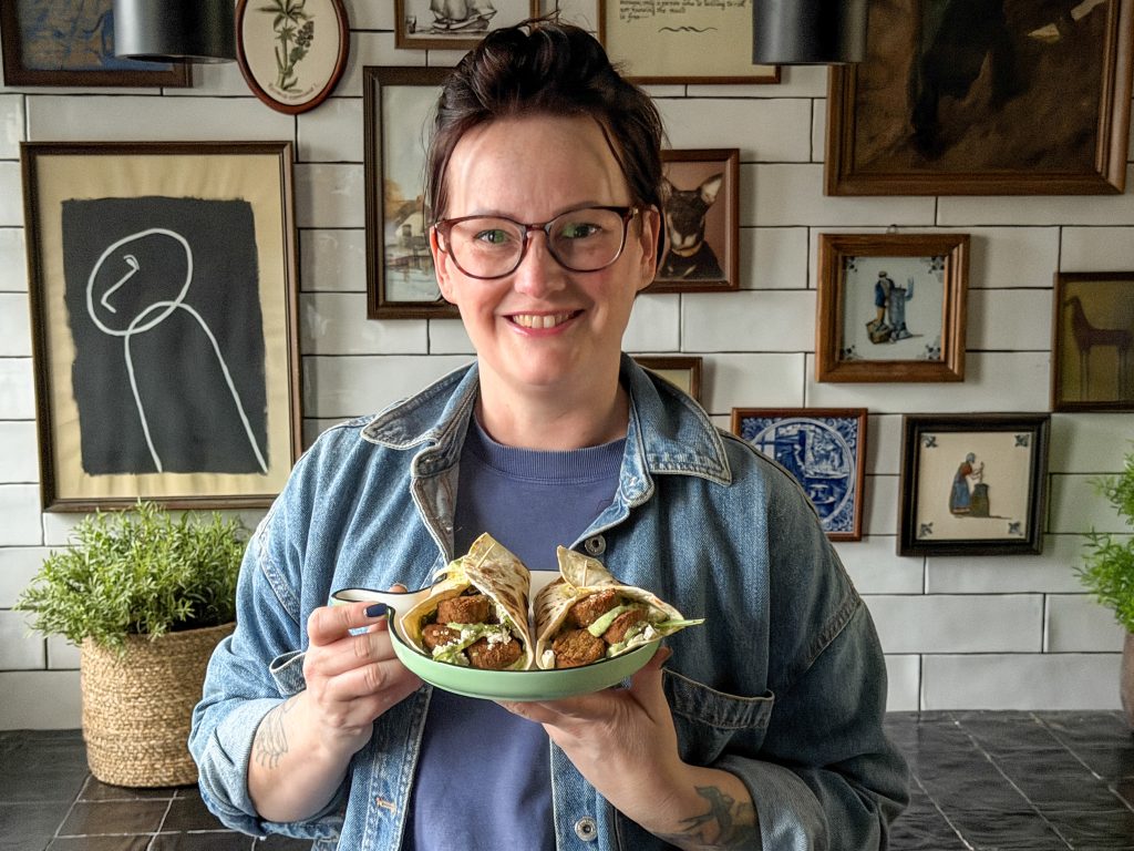 Marie Louise houdt een bord met wraps met falafel, sla en avocado-yoghurtdip vast in de keuken