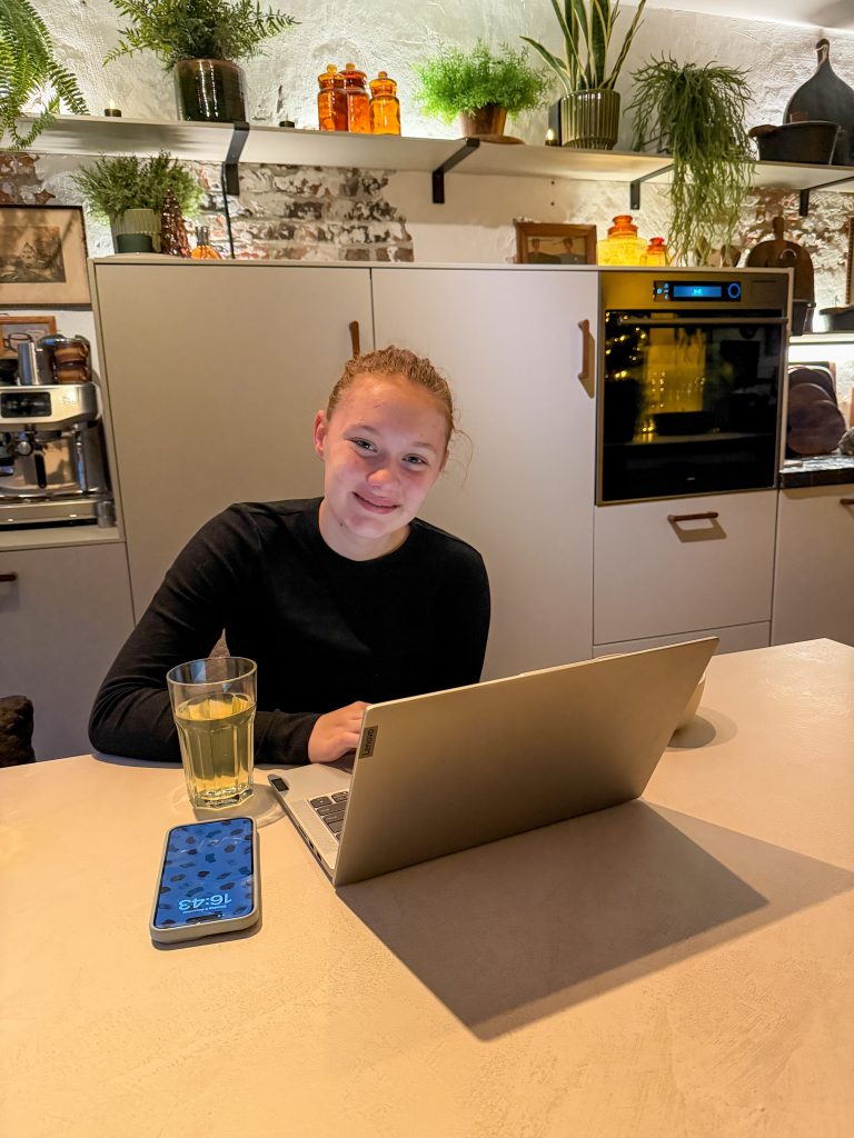 Amaranthe zit met haar laptop aan de keukentafel terwijl ze schoolwerk maakt.