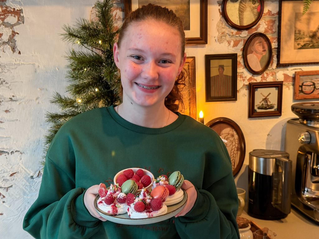 Amaranthe houdt een schaal met feestelijke pavlova's met frambozen vast in kersteuken