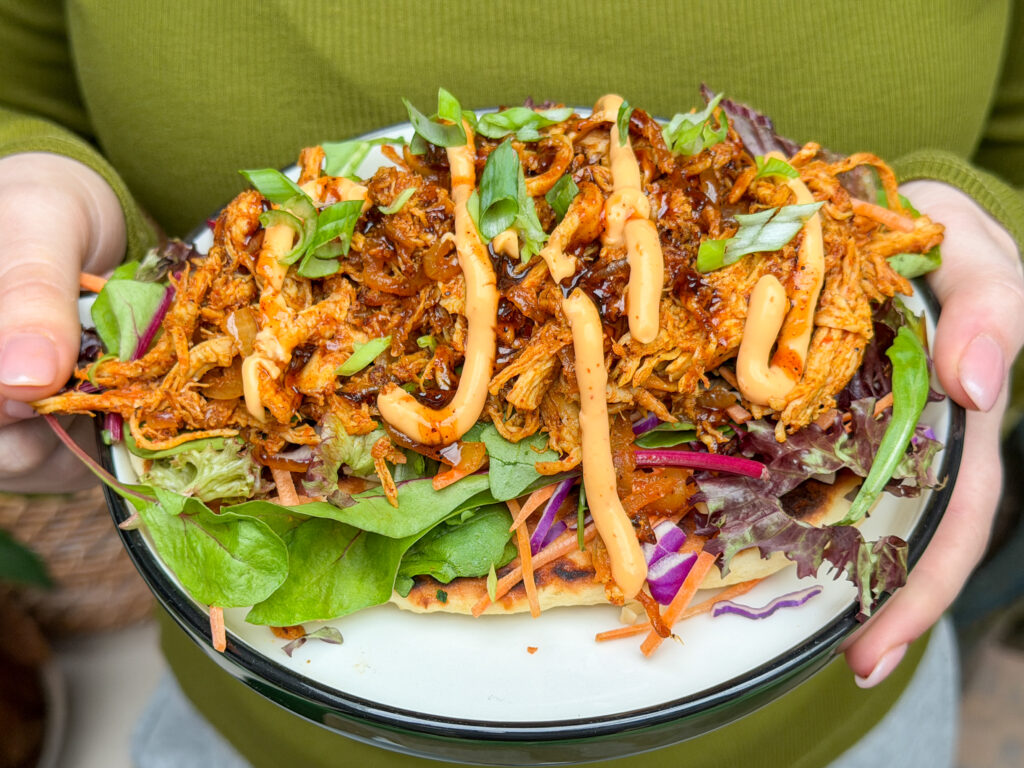 Flatbread met pulled chicken op bord wordt vastgehouden