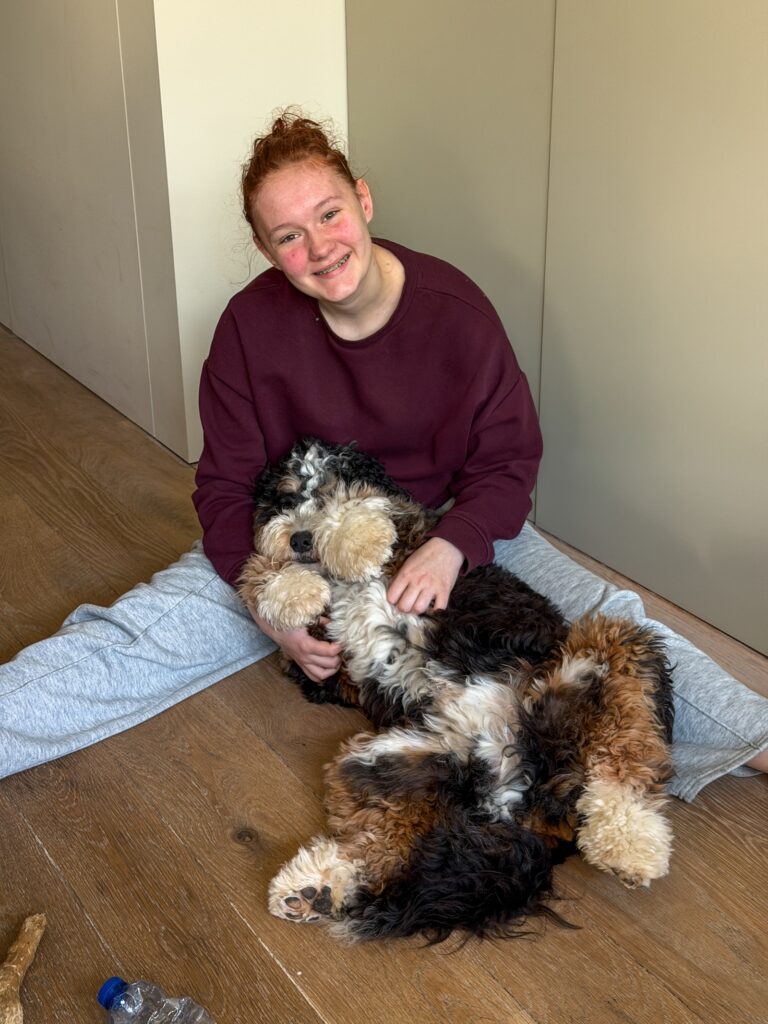 Amaranthe zit op de houten vloer met Legend op zijn rug in haar armen.