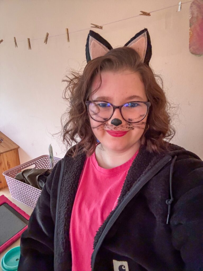 Beaudine met katten oortjes en geschminkt gezicht voor een selfie.