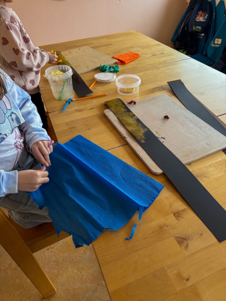 Knutselen aan tafel met gekleurd papier en knutselspullen.