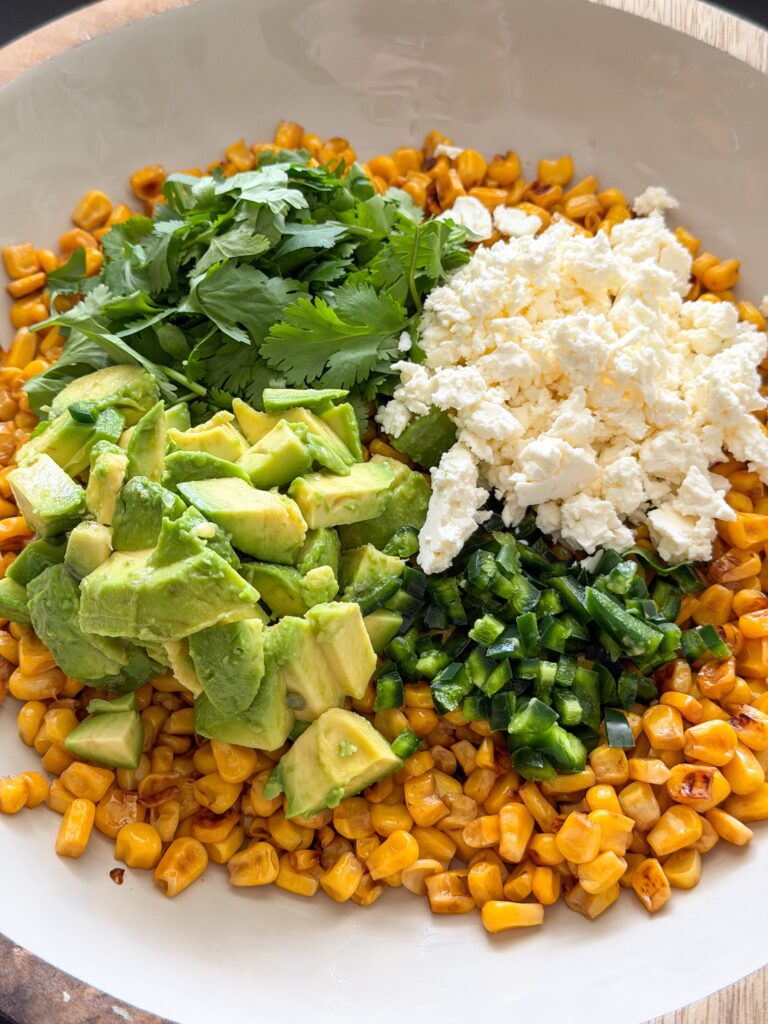 Gebakken mais, avocado, feta, koriander en jalapeño samenvoegen voor de salade