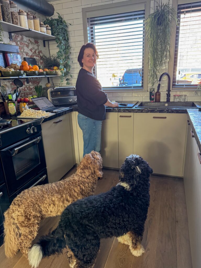 Marie Louise staat in de keuken te koken terwijl Legend en Teun naast haar wachten op de houten vloer.