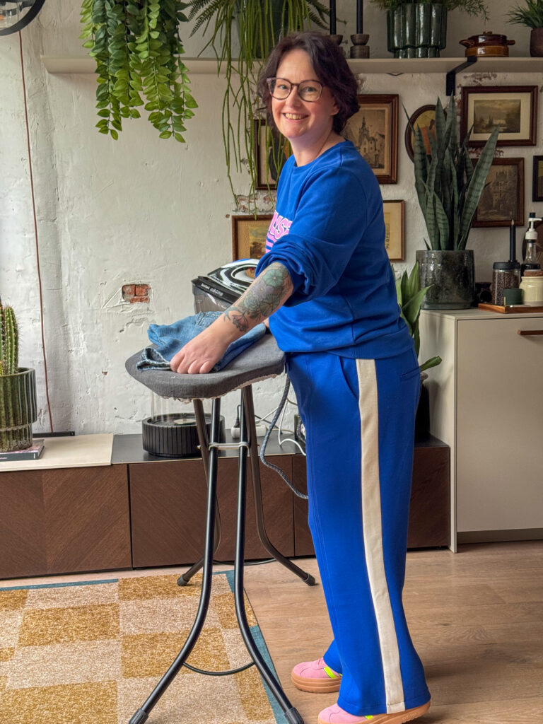 Marie Louise strijkt kleding op een strijkplank in de woonkamer.