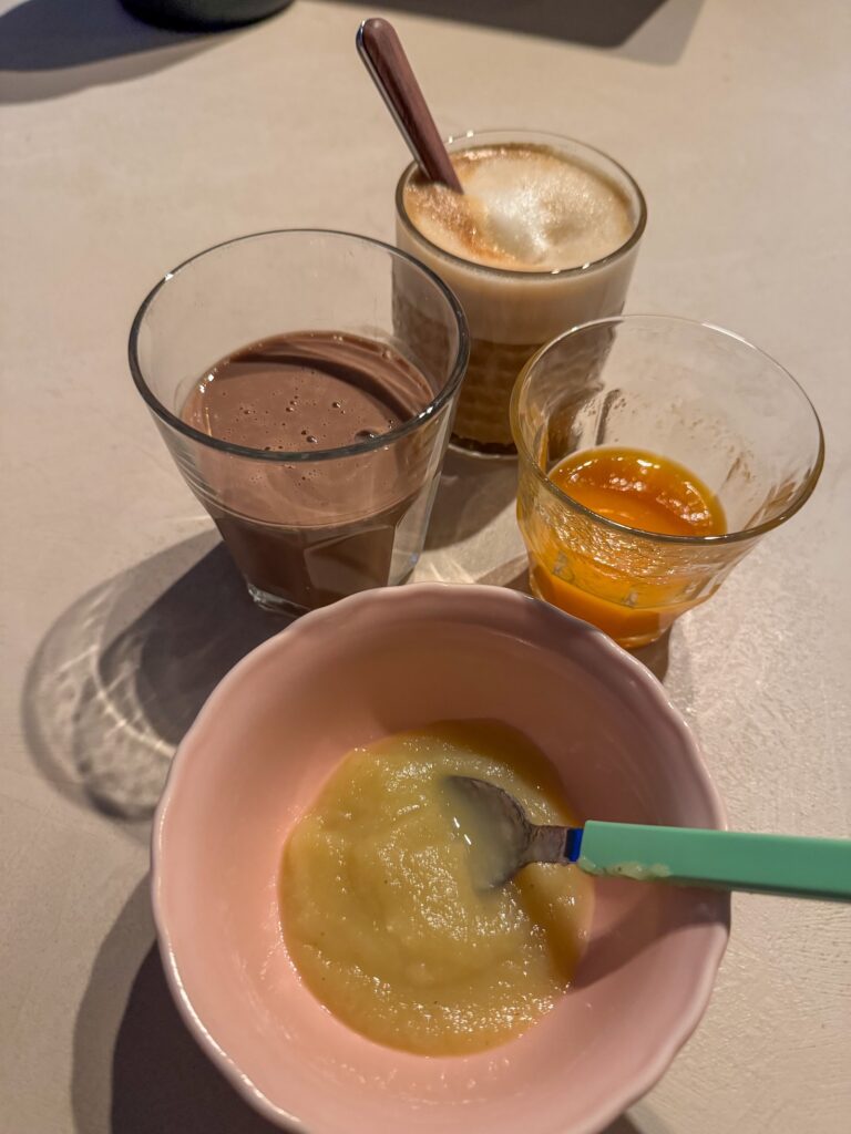 Ontbijt met appelmoes in een roze kom, chocolademelk, cappuccino en een glas vers sap op het aanrecht