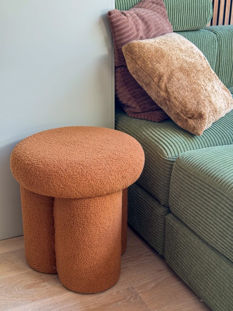 Oranje poef naast de groene bank met sierkussens in de woonkamer