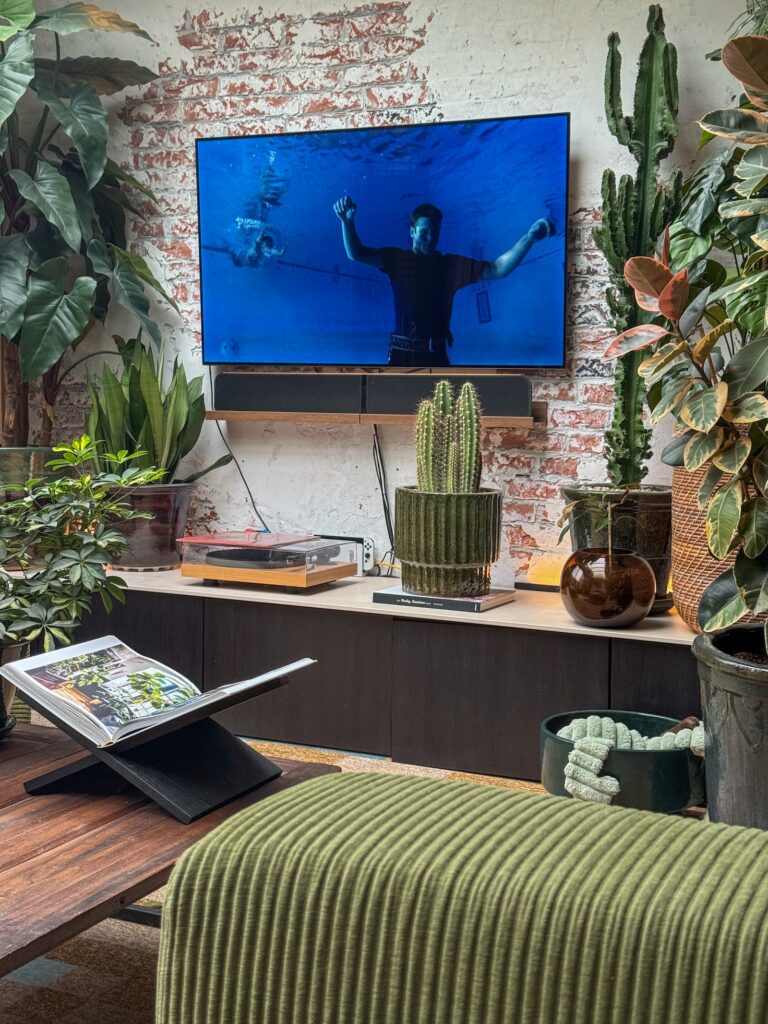 Woonkamer met veel groene planten en bakstenen muur terwijl op de tv een film met onderwaterscène wordt afgespeeld