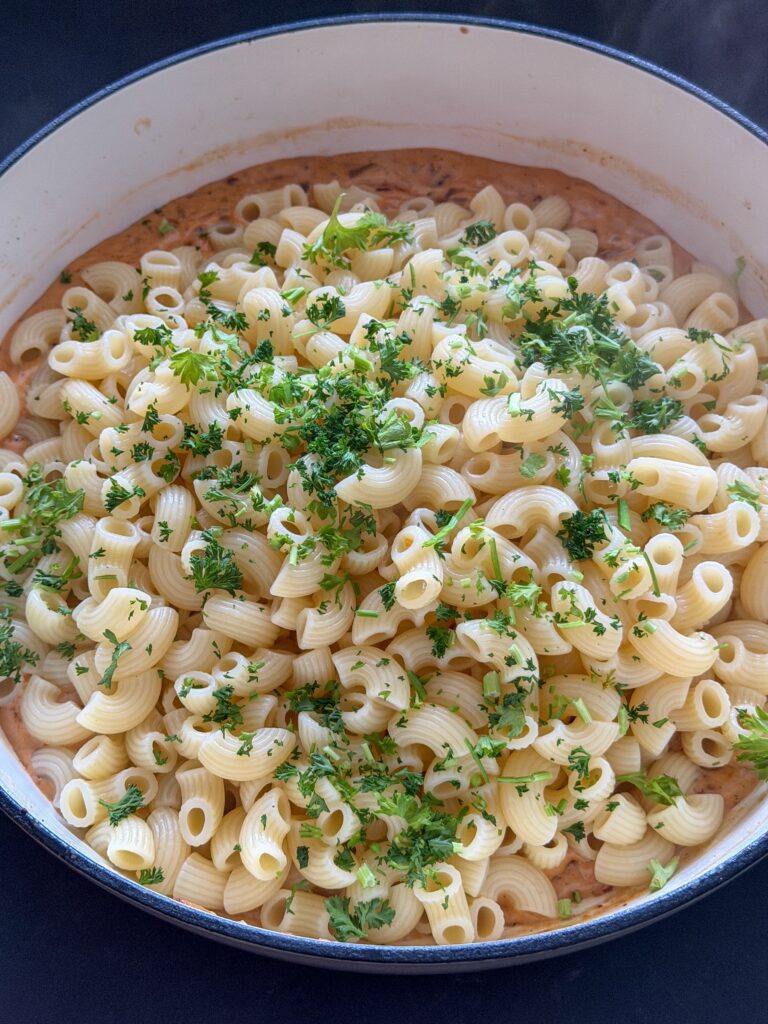 Gekookte macaroni en peterselie toevoegen aan de roomsaus