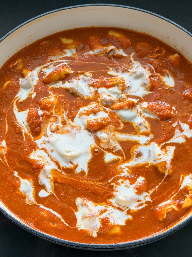 Room toevoegen aan de tortellini soep voor een romige tomatenbouillon