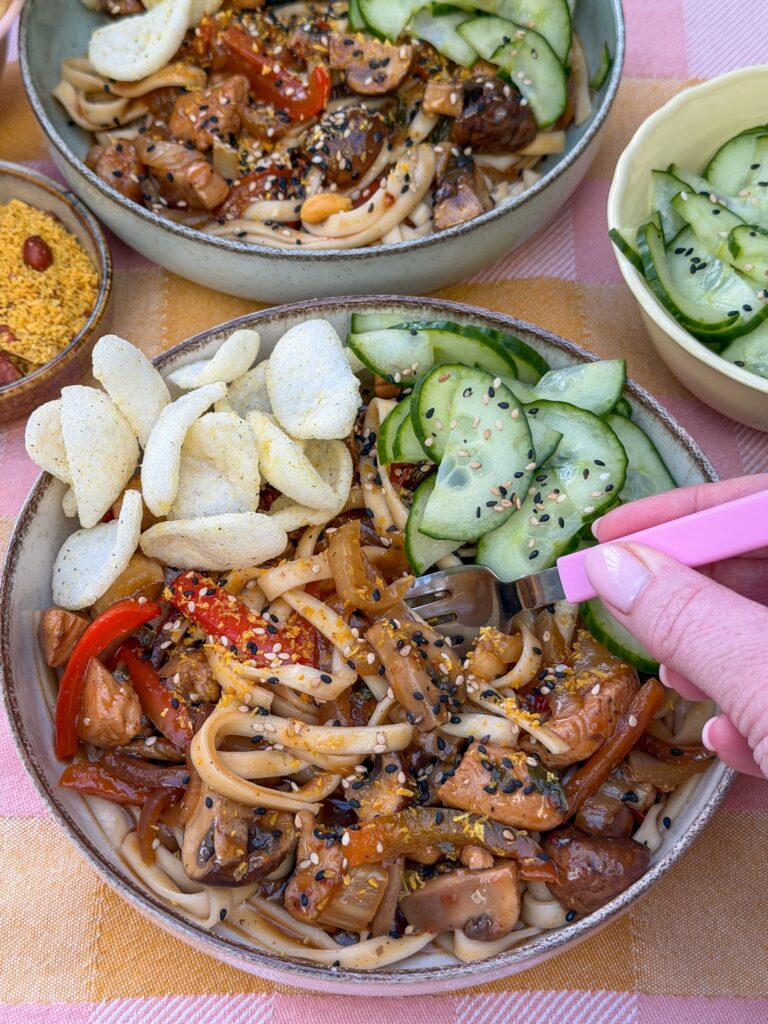 udon noedels met kip geserveerd met komkommer salade en kroepoek