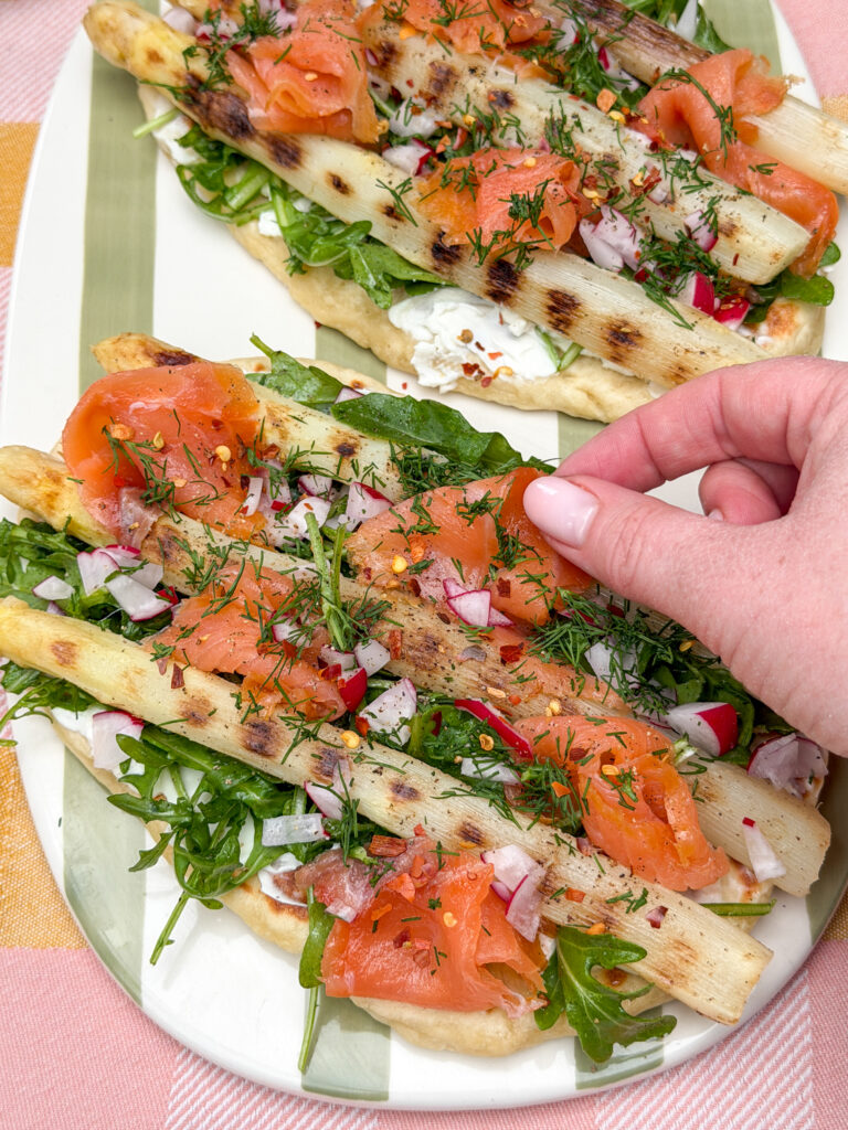 hand pakt stukje zalm van flatbread met witte asperges en zalm