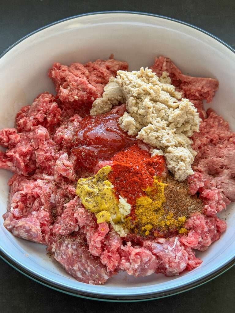 ingrediënten voor gehaktballen maken met gehakt, paneermeel, kruiden, ketchup en mosterd in een kom