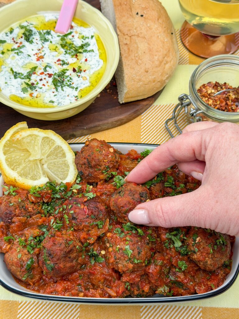 hand pakt gehakt balletjes in tomatensaus
