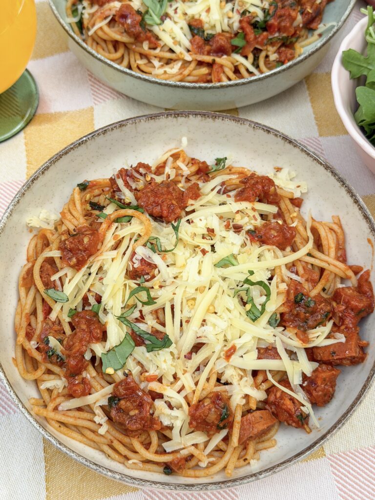 Close-up van pasta met chorizo in tomatensaus met kaas en basilicum