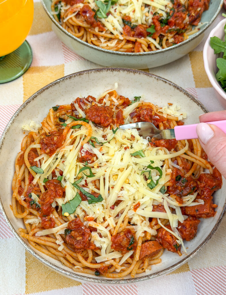 Pasta met chorizo in tomatensaus op bord met geraspte kaas en basilicum