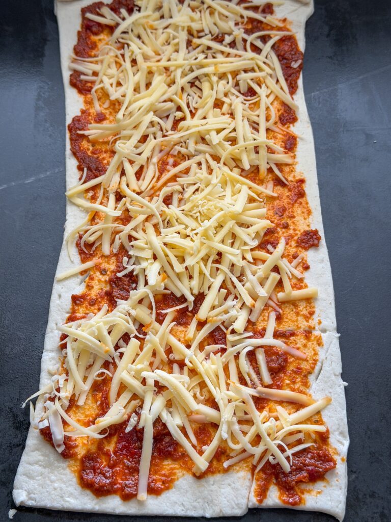 Croissantdeeg ingesmeerd met pesto en bestrooid met geraspte kaas