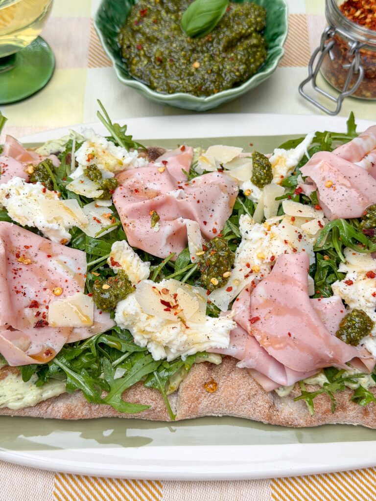 Pinsa met mortadella en pesto geserveerd met extra pesto en chilivlokken