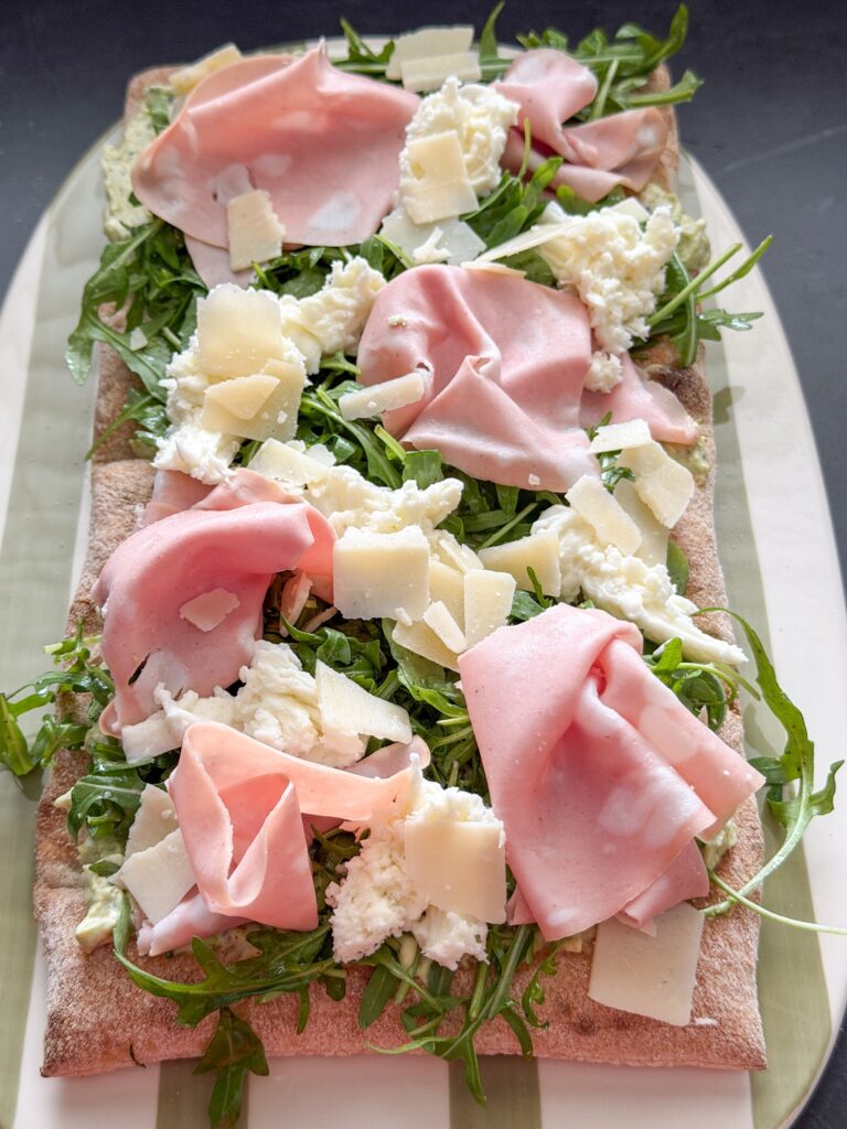 Pinsa bodem beleggen met pesto-roomkaas, rucola, mortadella en mozzarella