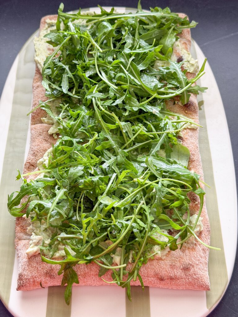 Pinsa bodem belegd met pesto-roomkaas en frisse rucola