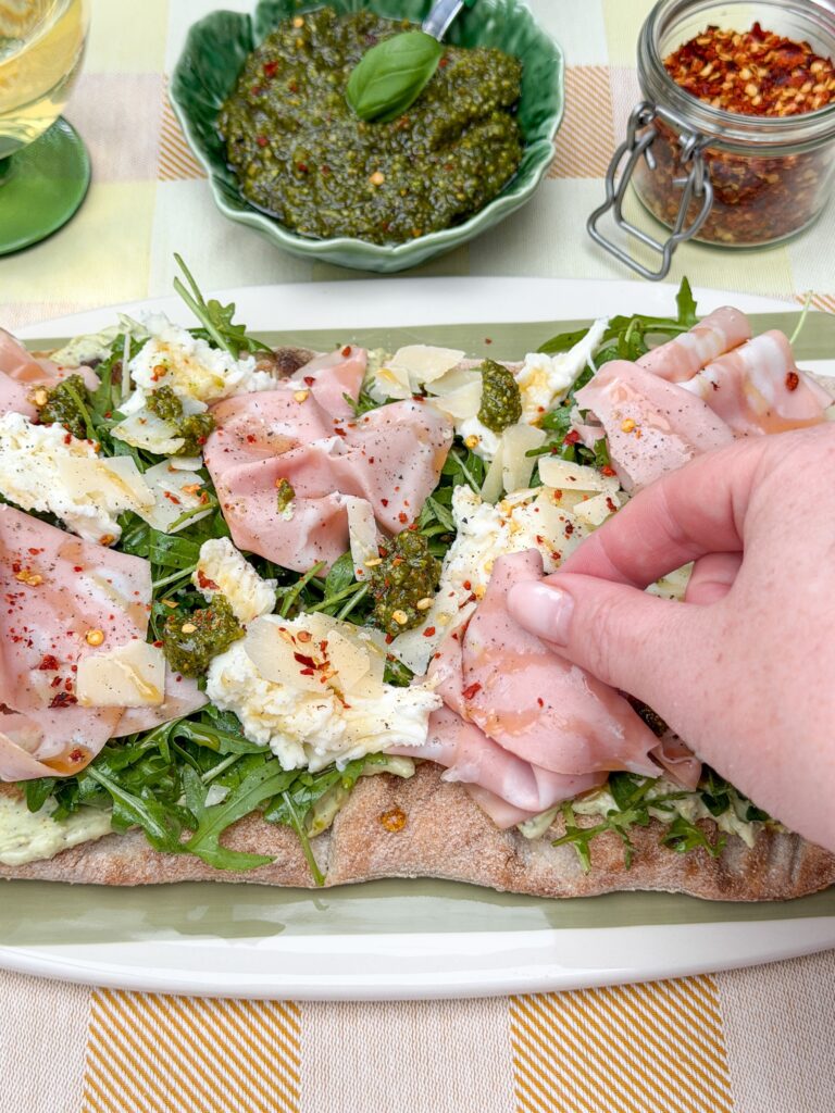 Hand pakt een stuk pinsa met mortadella
