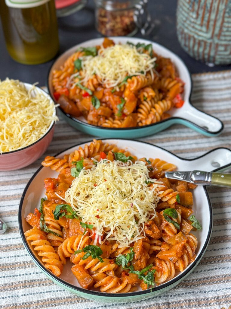 Een bord met heerlijke pasta met aubergine en tonijn, afgemaakt met verse basilicum en geraspte kaas.