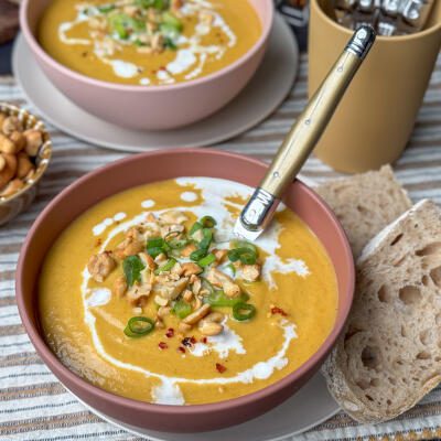 een kom vol heerlijke bloemkoolsoep met zoete aardappel, gele curry en afgetopt met bosui, cashewnoten en chilivlokken