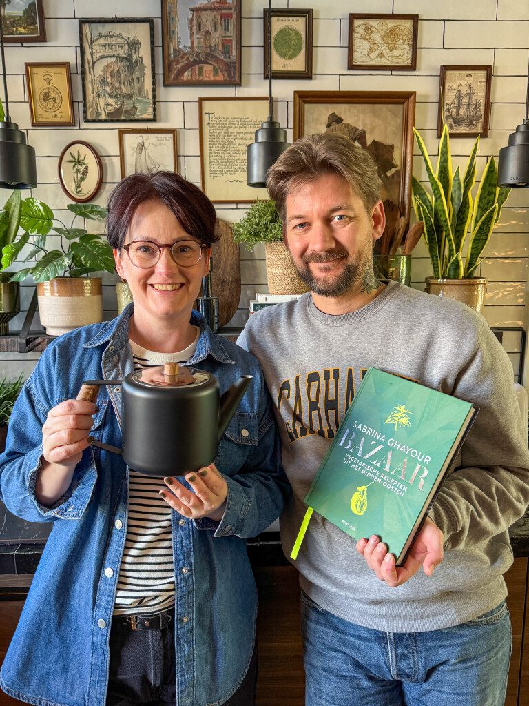 Marie Louise en Jan Willem staan in de keuken met een kookboek en een theepot. 