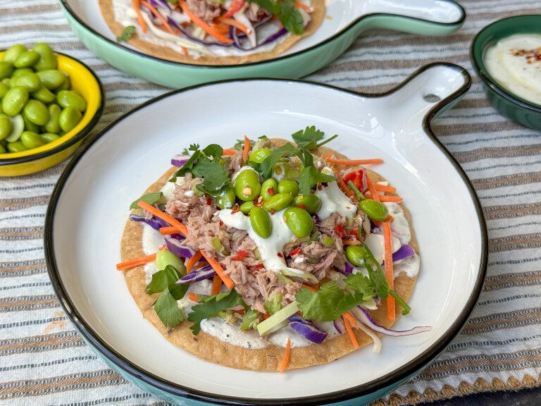 Tostada’s met tonijn en avocado – fris, knapperig en makkelijk! tostada met tonijn en avocado, sojaboontjes en koolmix geserveerd met een frisse limoen – yoghurtdipsaus geserveerd op een bord.
