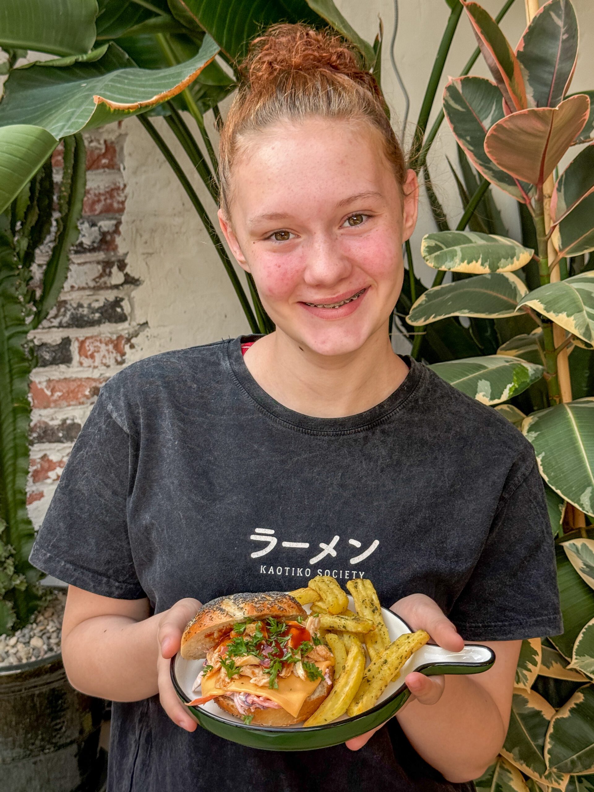 pulled chicken broodje met hot honey saus - geserveerd door Amaranthe met frietjes op een rond bord