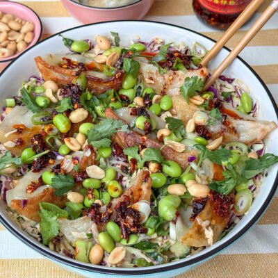 Gyoza salade: frisse Aziatische salade met pittige dressing gyoza salade met edamame en pittige dressing geserveerd in witte schaal met pinda's en crispy chili olie