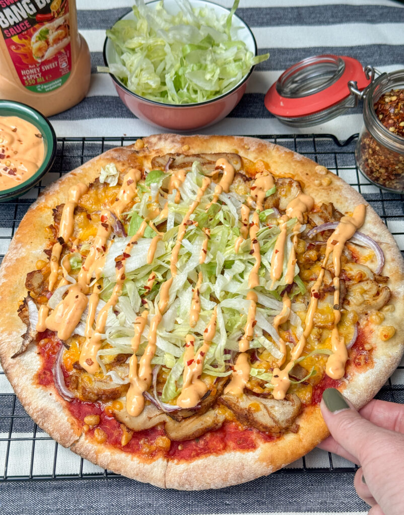 hand pakt punt pizza met kip kebab, ijsbergsla en bang bang saus van rooster